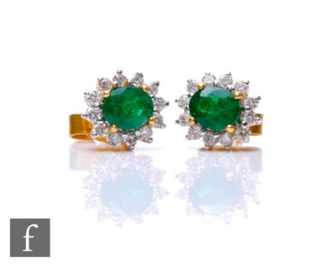 A pair of 18ct emerald and diamond stud earrings, central oval emerald within twelve stone brilliant cut diamond surround, le