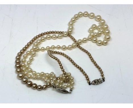 A pearl necklace with white gold clasp set with a small diamond, together with another with white metal clasp. 