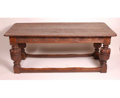 An antique oak refectory table, in the Elizabethan style, having a two plank top, blind carved frieze, and raised on heavy cu