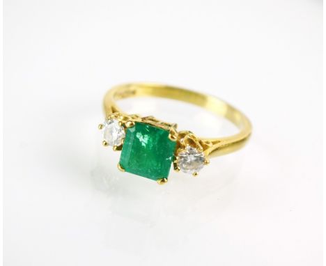 An 18ct gold three stone emerald and diamond ring, designed as a central square faceted emerald flanked to each side by a bri