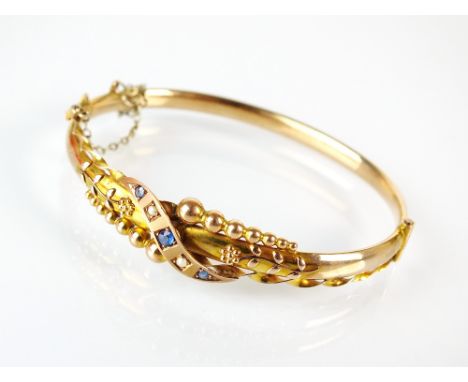 A split seed pearl and blue paste set hinged bangle, with decorative bead and floral detail, stamped '9ct', weight 6.3g