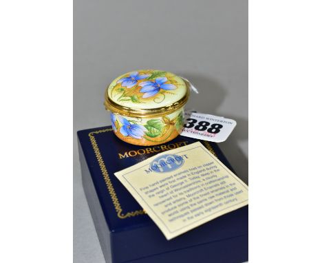 A BOXED MOORCROFT ENAMELS TRINKET BOX, of circular form, decorated with violets on a pale yellow ground, printed marks to bas