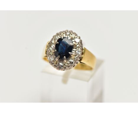 A YELLOW METAL SAPPHIRE AND DIAMOND CLUSTER RING, centering on an oval cut deep blue sapphire, in a six claw setting, within 