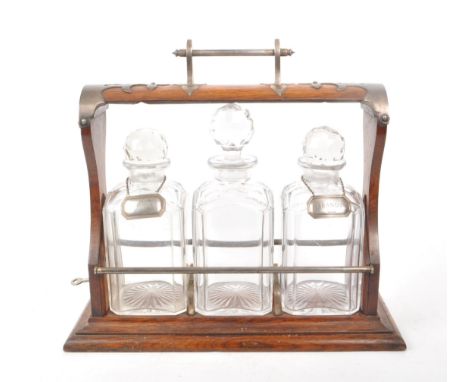 A wooden early 20th/ 19th century tantalus with metal detailing. Comes with three cut glass decanters and two hallmarked silv