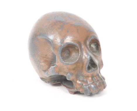 A vintage 20th century small bronzed metal cast skull. Showing signs of a painted coating to the surface. Featuring a printed