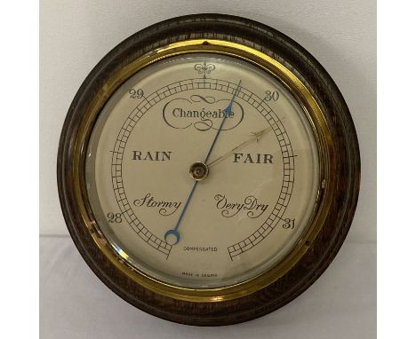 A vintage brass framed wall hanging barometer on turned wooden plinth.  Approx. 22cm diameter.