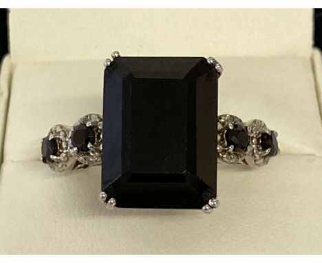 A silver modern design statement dress ring set with black spinel. Large central emerald cut stone with two small round cut s