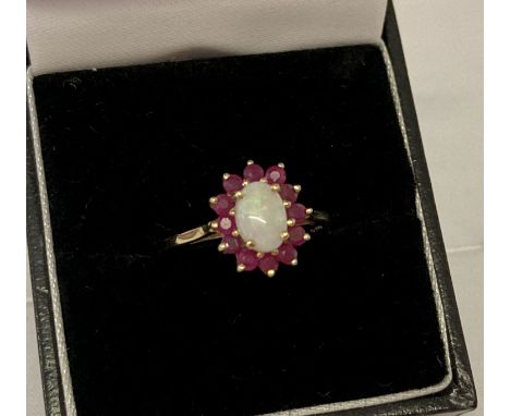 A 9ct gold opal and ruby dress ring, size N½. A central oval cut opal surrounded by 12 round cut rubies. Marked 375 with full