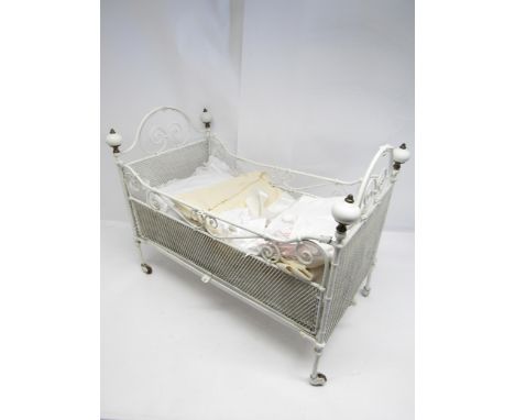 A white painted wrought iron dolls cot bed with mesh sides and ceramic finials, on castors, 69cm long x 38cm wide x 52cm deep