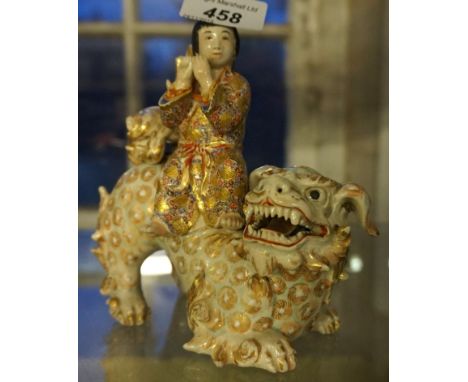 A Japanese satsuma model of a man playing a musical instruments seated on a shishi lion.