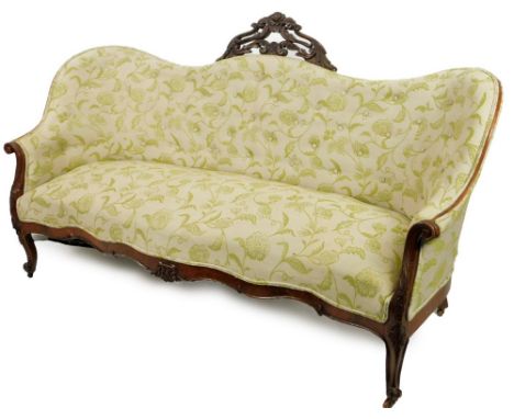 A Victorian walnut serpentine sofa, surmounted by an arrangement of carved scrolls and flowerheads, upholstered in green and 