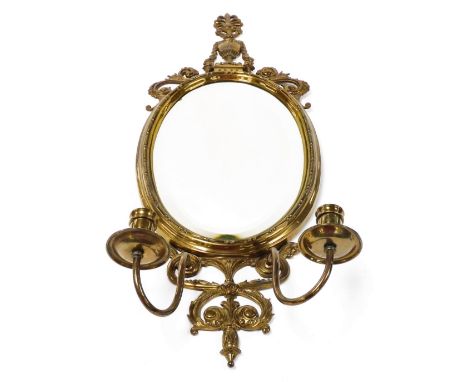 A late 19thC brass wall mirror, with oval mirror plate, brass urn finial and scroll supports, with two candle sconces, 72cm h