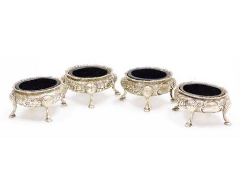 A set of four Victorian silver salts, with blue glass liners, having chased rim with repousse floral and cartouche sides, on 