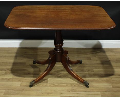 A Regency mahogany rounded rectangular breakfast table, moulded tilting top, turned pillar, hipped sabre legs, brass casters,