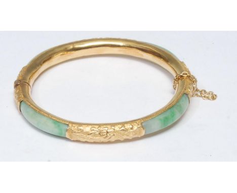 A jade inset yellow metal hinge bangle,  four panels of stained jade green stone, inset to a tubular yellow metal body, compr
