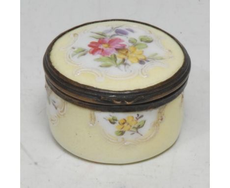 A Rococo design enamel circular snuff box or bonbonniere, painted in polychrome with country flowers in raised C-scroll borde
