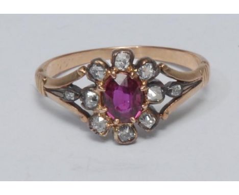 A diamond and ruby cluster ring, central oval vibrant red ruby surrounded by eight old cushion and baguette cut diamonds, tot