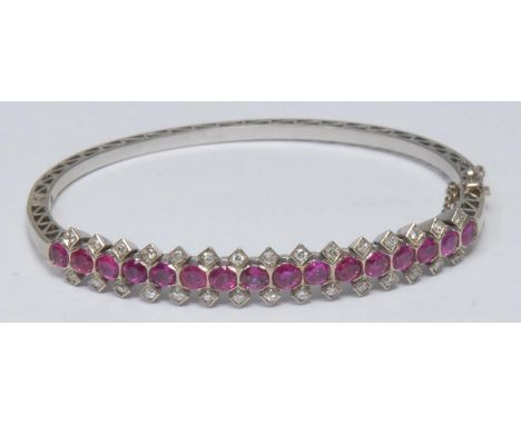 A ruby and diamond hinge bangle, linear set with sixteen oval pinky red Burmese rubies, each divided by a pair of round brill