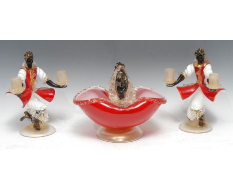 A pair of Murano glass figural Blackmoor two light candle holders, both kneeling wearing red coats, holding the sconces in th