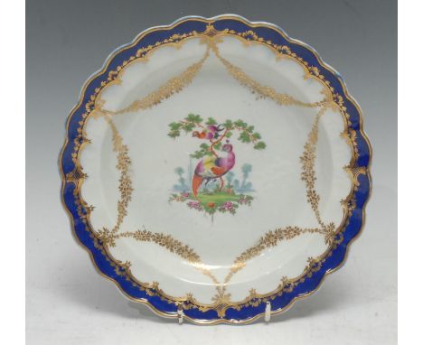 A Worcester shaped circular plate, painted with two exotic birds in a landscape surrounded by gilt swags of flowers, cobalt b