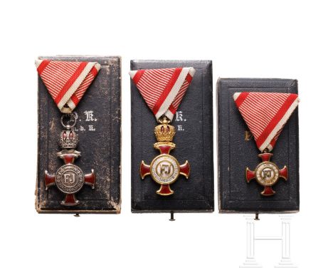 Drei Verdienstkreuze im Etui  Verdienstkreuz mit Krone in vergoldeter Ausführung, beidseitig rot emailliert, Bandring gepunzt