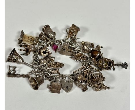 A silver curb link bracelet mounted with a large collection of silver charms including a key, bells, miniature clock, glass c