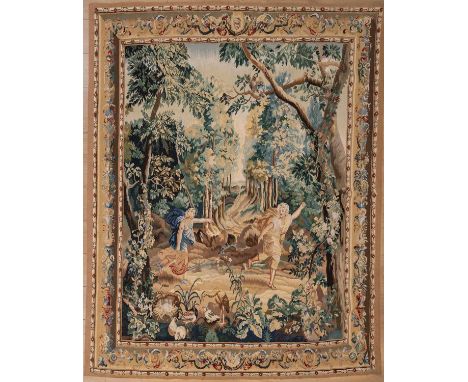 A 17th century style Continental tapestry depicting two classical figures in a woodland glade within a border of scrolling fo