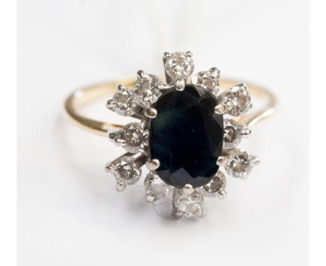 A sapphire and diamond yellow gold cluster ring, the centre dark blue sapphire approx 8 mm by 6 mm, the twelve diamond surrou