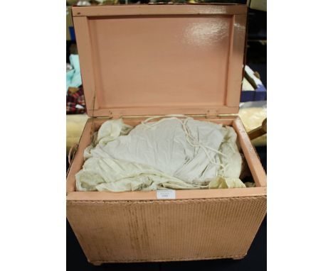 An early 20th Century pink wicker work linen basket containing a collection of textiles