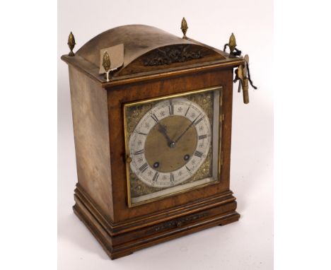 A German walnut cased mantel clock, the square dial with silvered chapter ring, the arched case with pinecone finials to the 
