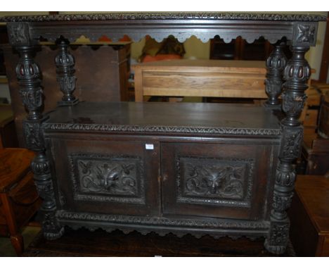 A late 19th century heavily carved ebonised oak buffet, having twin Green Man mask carved doors, raised on carved cup and cov