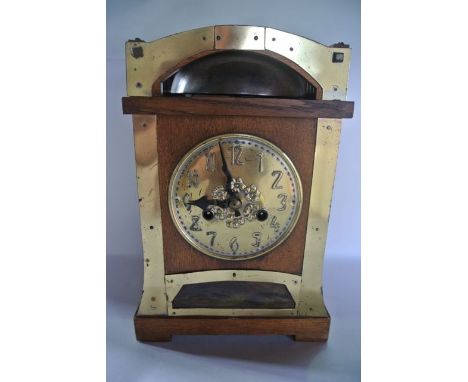 An Arts & Crafts mantle clock in oak with applied brass detail, with embossed brass dial over a marbled glass panel, set bene