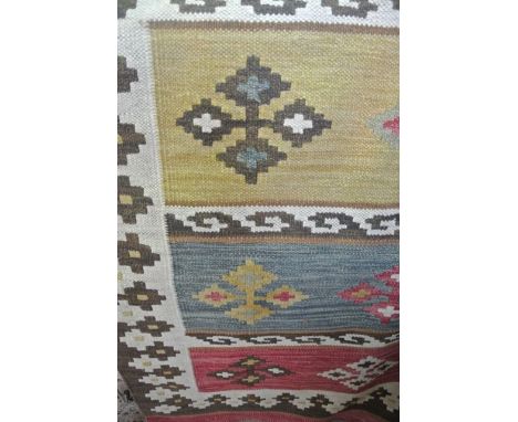 A Kelim wool carpet in various coloured bands, pinks, blues, ochre, etc, overlaid with geometric detail, set within running b