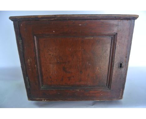 A small vintage stained pine cupboard of squared form, the front panel hinged door revealing a bank of two drawers with flush