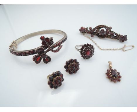 A late Victorian garnet hinged bangle, centred with two floral motifs on the overlapping shoulders, with safety chain, in gil