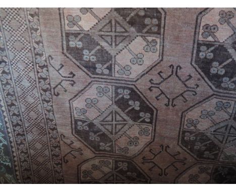 An Afghan red wool carpet with octagonal medallion panels, set within running borders, 315 x 225 cm