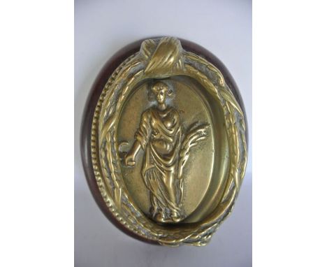 A cast brass door knocker of oval form depicting Harvest, a figure standing clenching wheat and a scythe, set within a steppe