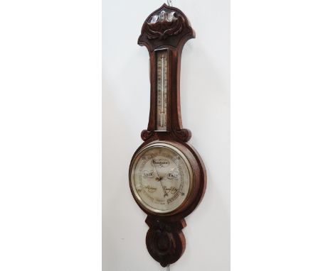 An early 20th century oak aneroid barometer - carved with foliage, with a silvered dial and incoporating a thermometer