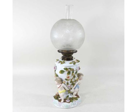 An early 20th century Sitzendorf porcelain oil lamp, encrusted with coloured flowers, on cherub supports, with a Young's burn