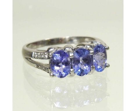 A 9 carat white gold, three stone tanzanite ring, with diamond set shoulders, 4.5g, size R, boxed