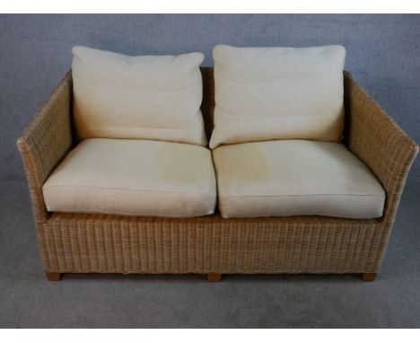 A contemporary two seater wicker conservatory sofa with loose cushions raised on block feet. H.72 W.148 D.87cm. 