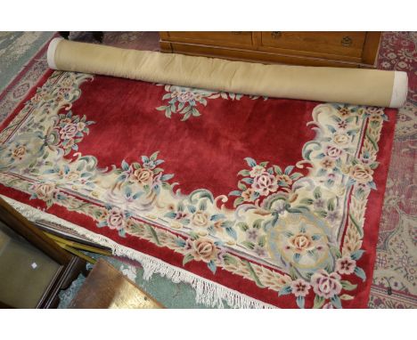 A large carpet decorated with flora in hues of blue, green, brown and cream on a red ground.