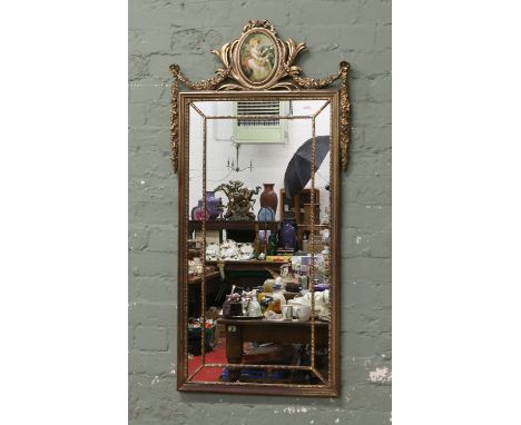 An ornate gilt framed wall mirror decorated with garlands and swags and oval portrait of a lady picking roses.