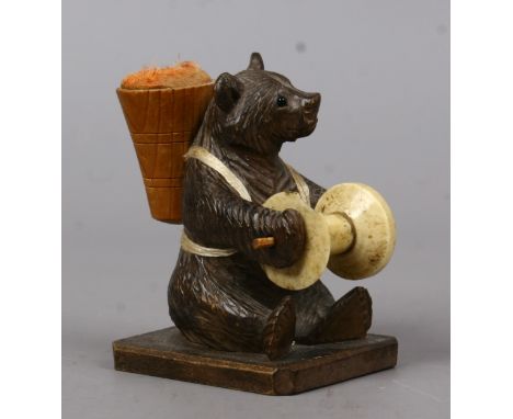 A Black Forrest pin cushion and cotton bobbin carved in the for of a seated bear.