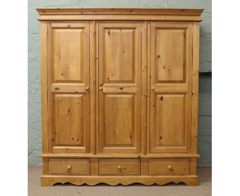 A panelled pine triple wardrobe raised on a three drawer plinth.
