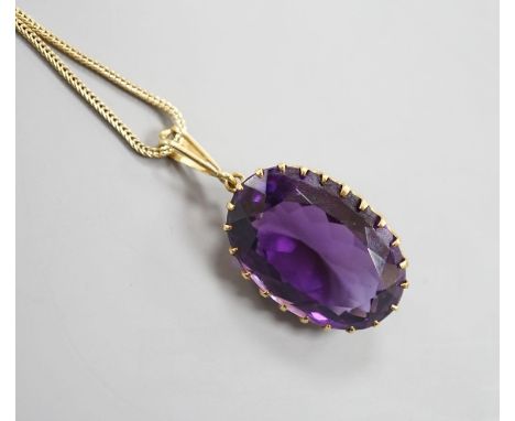 An early 20th century yellow metal mounted oval cut amethyst pendant, overall 37mm, on a yellow metal fine link chain, 49cm, 