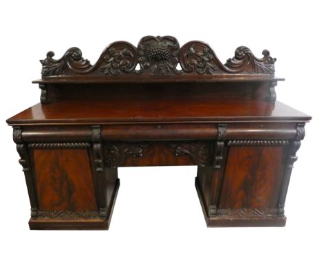 A George IV flame and carved mahogany pedestal sideboard, the back piece deeply carved with fruit, over a shelf with S scroll