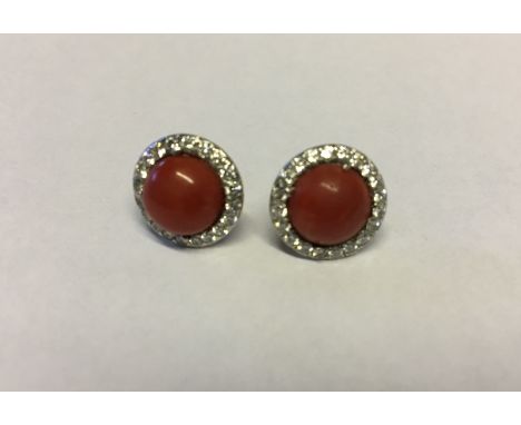 A PAIR OF 18CT WHITE GOLD, RED CORAL AND DIAMOND STUD EARRINGS The round coral cabochons claw set to a surround of round cut 