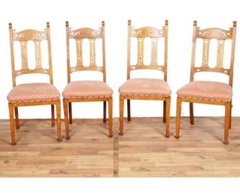 A set of four early 20th Century oak Arts and Crafts chairs, with carved and pierced spats, and seat pads upholstered in a pi