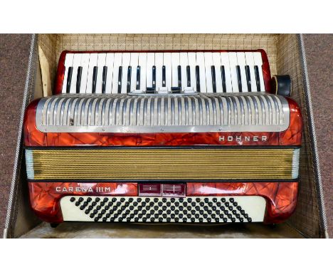 A Hohner Carena IIIM, red marble effect cased piano accordion with a travel case